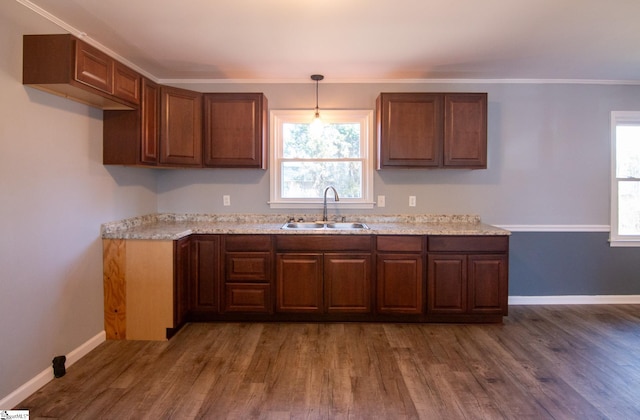 kitchen with wood finished floors, a sink, baseboards, ornamental molding, and brown cabinetry