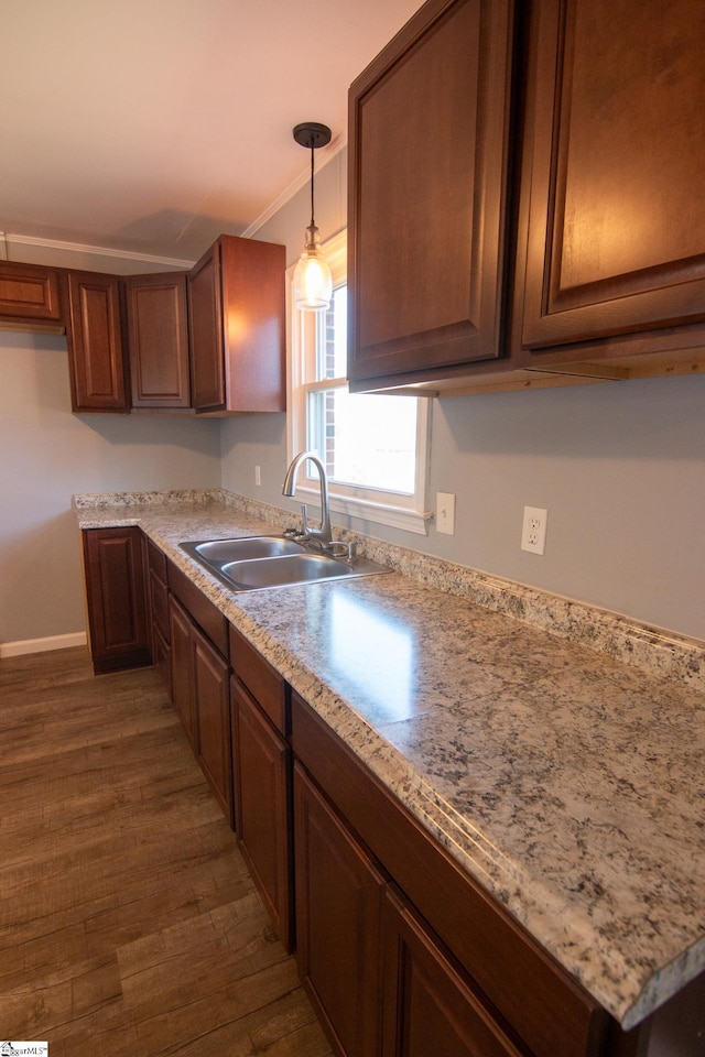 kitchen with dark wood-style floors, ornamental molding, decorative light fixtures, light countertops, and a sink