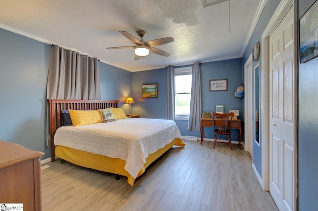 bedroom with a textured ceiling, light wood-style flooring, baseboards, attic access, and crown molding