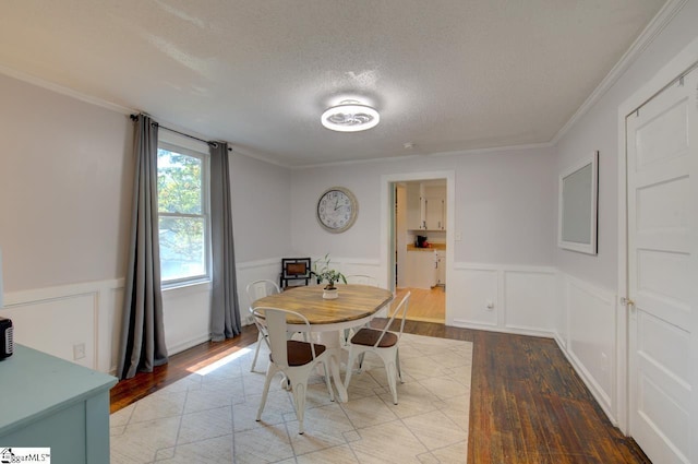 dining space featuring light wood-style flooring, crown molding, a textured ceiling, and wainscoting