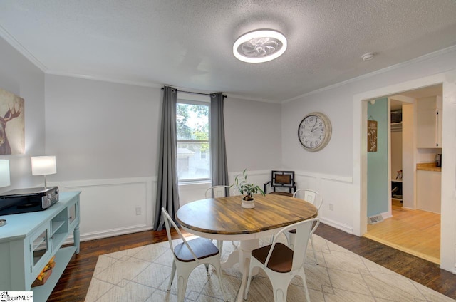 dining area featuring a wainscoted wall, a textured ceiling, ornamental molding, and wood finished floors