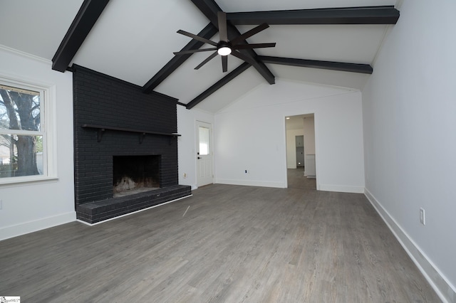 unfurnished living room featuring beamed ceiling, a brick fireplace, wood finished floors, and baseboards