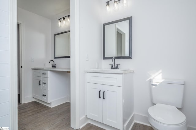 bathroom with two vanities, a sink, toilet, and wood finished floors