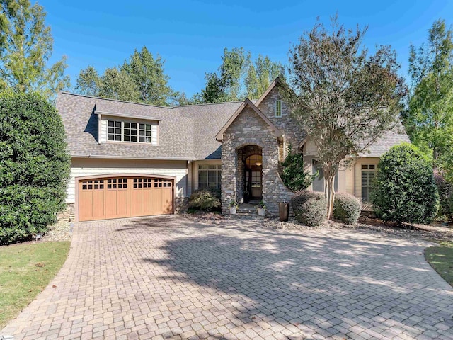 view of front of home with stone siding, a shingled roof, and decorative driveway