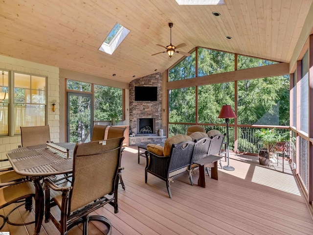 sunroom with a ceiling fan, vaulted ceiling with skylight, wood ceiling, and a fireplace