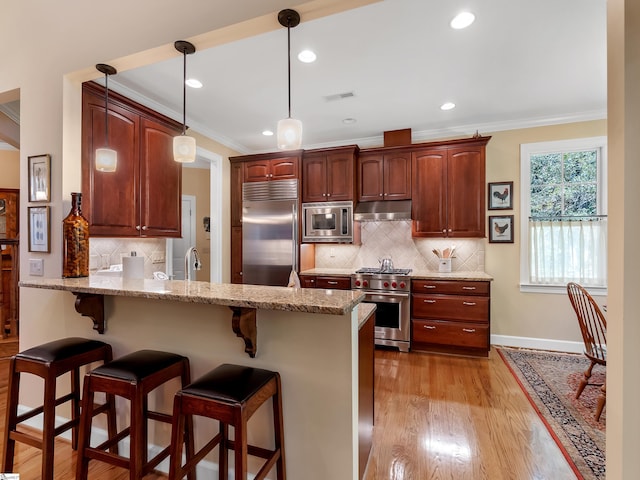 kitchen with a breakfast bar, ornamental molding, a peninsula, built in appliances, and under cabinet range hood