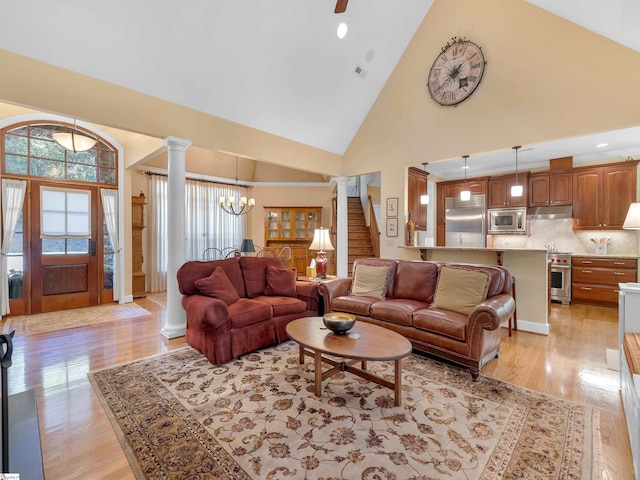 living area with high vaulted ceiling, stairway, light wood-type flooring, decorative columns, and an inviting chandelier