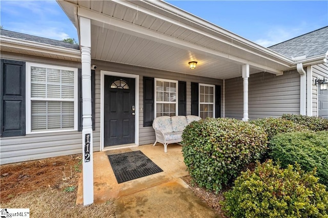 entrance to property featuring covered porch and roof with shingles