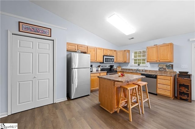 kitchen featuring appliances with stainless steel finishes, a breakfast bar area, wood finished floors, a center island, and vaulted ceiling