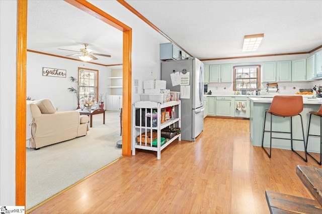 kitchen featuring a breakfast bar area, ornamental molding, freestanding refrigerator, light countertops, and green cabinetry