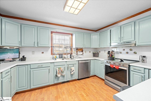 kitchen with appliances with stainless steel finishes, blue cabinetry, light wood-type flooring, under cabinet range hood, and a sink