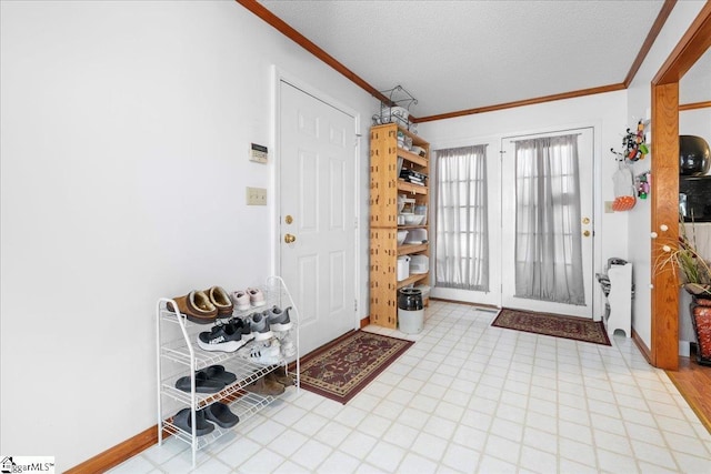 foyer featuring a textured ceiling, light floors, ornamental molding, and baseboards