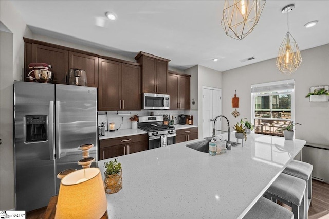 kitchen featuring stainless steel appliances, a breakfast bar, a sink, visible vents, and dark brown cabinets