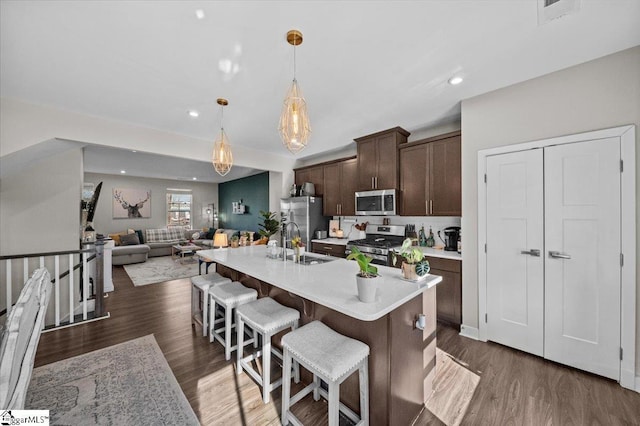 kitchen with stainless steel appliances, wood finished floors, dark brown cabinets, light countertops, and a kitchen bar