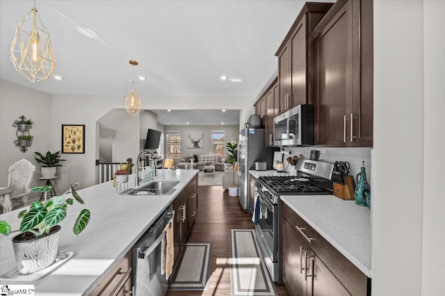 kitchen featuring stainless steel appliances, open floor plan, a sink, and dark brown cabinets