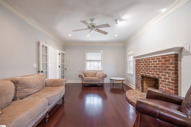 living room featuring ceiling fan, baseboards, ornamental molding, a brick fireplace, and hardwood / wood-style floors