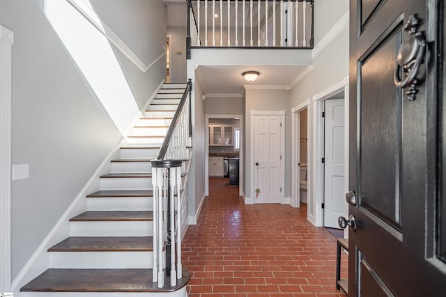 foyer entrance with baseboards, stairway, ornamental molding, brick floor, and a high ceiling