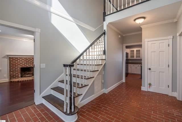 staircase featuring brick floor, crown molding, a towering ceiling, a brick fireplace, and baseboards