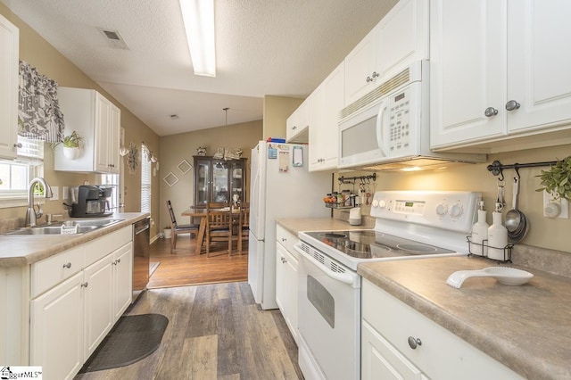 kitchen featuring white appliances, light wood finished floors, white cabinets, lofted ceiling, and a sink