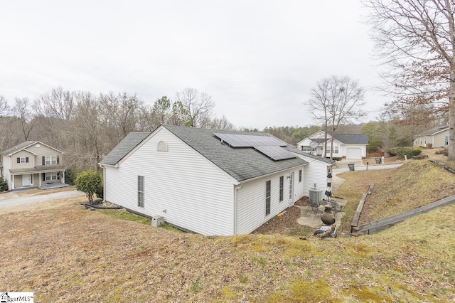 view of side of home featuring a shingled roof, cooling unit, a lawn, and solar panels