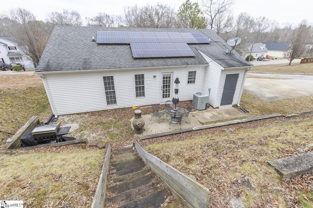 rear view of property with central air condition unit, a patio area, a shingled roof, and solar panels