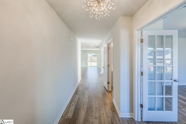 corridor featuring an inviting chandelier, baseboards, and wood finished floors