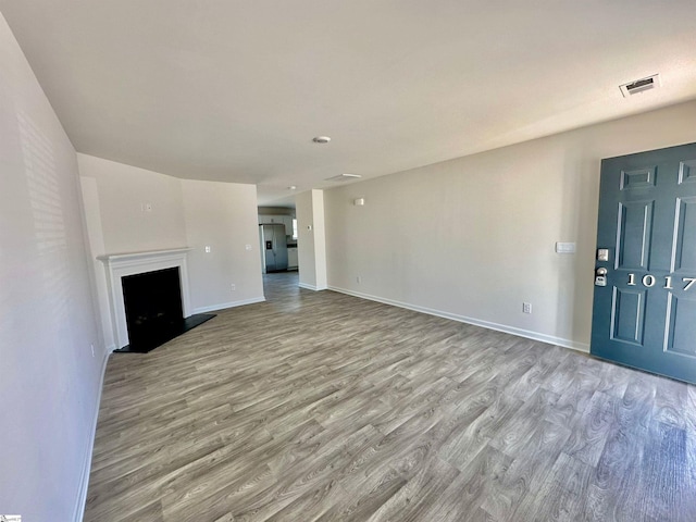 unfurnished living room featuring visible vents, a fireplace, baseboards, and wood finished floors