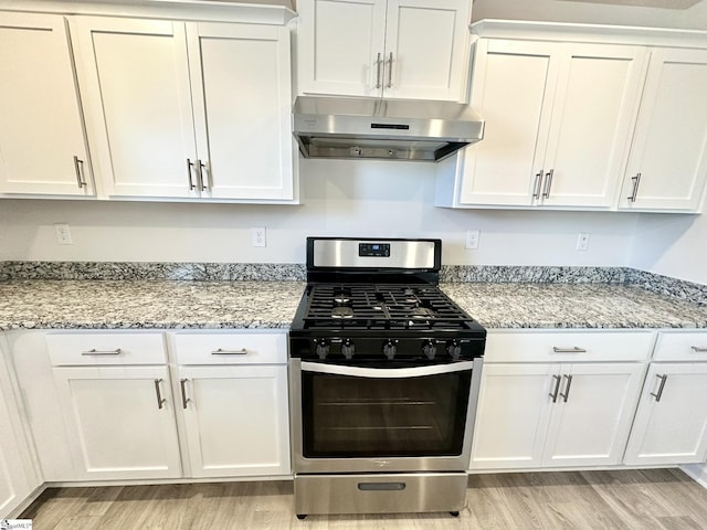 kitchen featuring gas range, light stone countertops, light wood-type flooring, under cabinet range hood, and white cabinetry