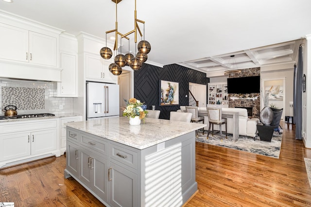 kitchen with high end fridge, stainless steel gas stovetop, light wood-type flooring, coffered ceiling, and under cabinet range hood