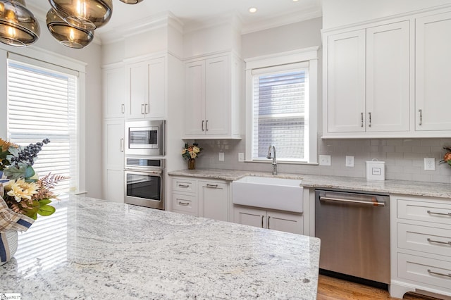 kitchen with crown molding, tasteful backsplash, appliances with stainless steel finishes, white cabinets, and a sink