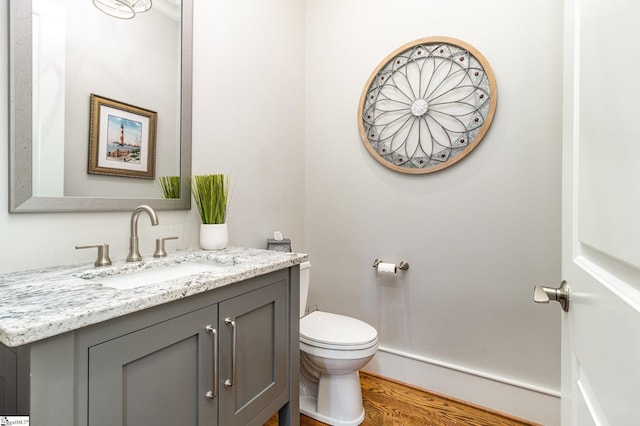 half bathroom featuring toilet, wood finished floors, and vanity