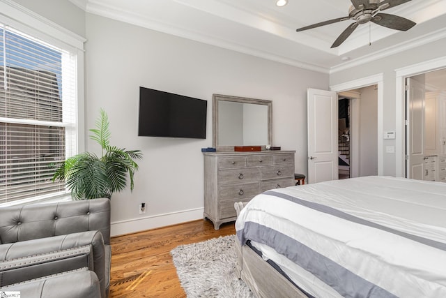 bedroom with baseboards, a tray ceiling, wood finished floors, and crown molding