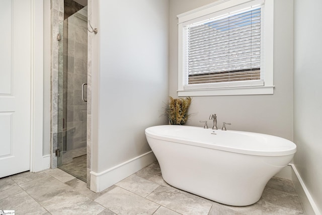 full bathroom with a stall shower, a freestanding tub, and baseboards