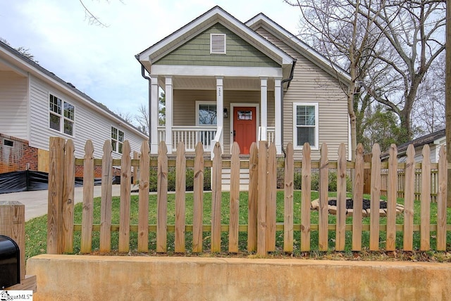 shotgun-style home with a fenced front yard and covered porch