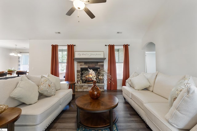 living room featuring arched walkways, dark wood finished floors, a fireplace, visible vents, and ceiling fan with notable chandelier