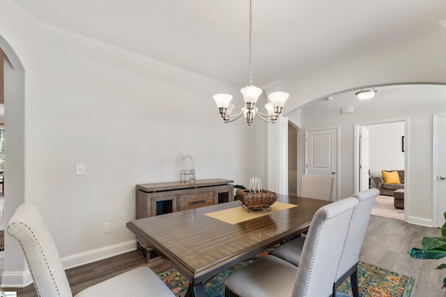 dining room with baseboards, arched walkways, a chandelier, and wood finished floors