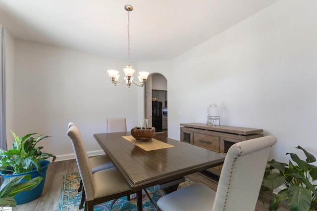 dining room featuring arched walkways, a notable chandelier, baseboards, and wood finished floors