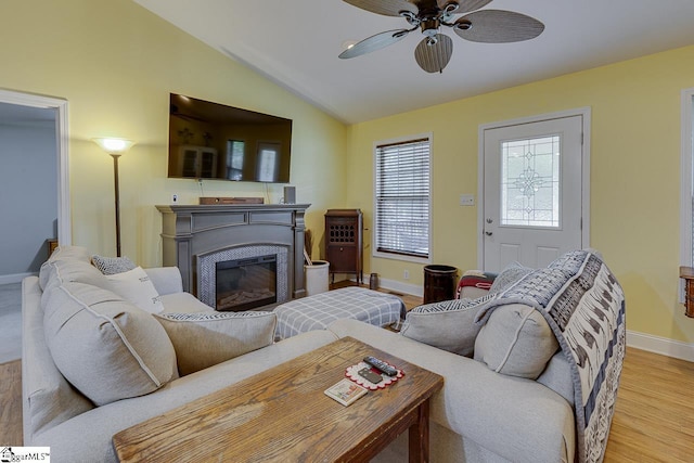 living area with ceiling fan, wood finished floors, baseboards, vaulted ceiling, and a glass covered fireplace