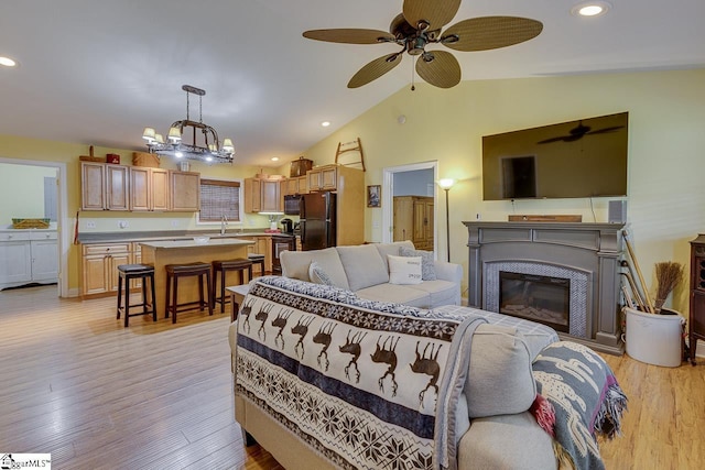 living area with ceiling fan with notable chandelier, light wood-type flooring, a glass covered fireplace, and recessed lighting