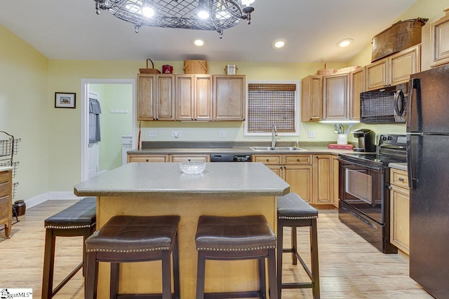 kitchen featuring light wood-style flooring, recessed lighting, a sink, a kitchen breakfast bar, and black appliances