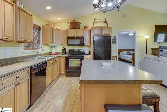 kitchen with a breakfast bar area, light wood finished floors, vaulted ceiling, a sink, and black appliances