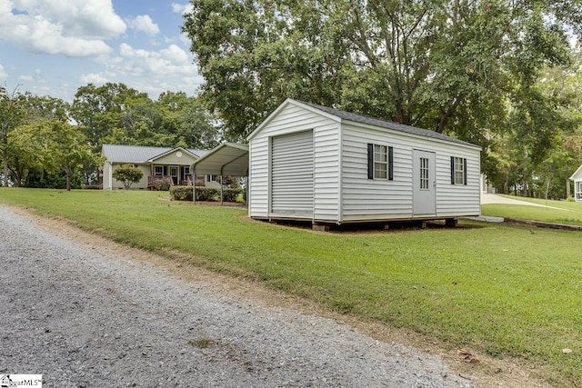 view of outdoor structure with driveway, a carport, and an outbuilding