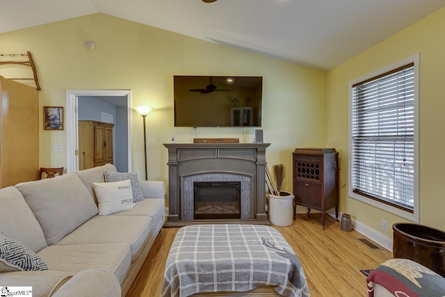 living area featuring vaulted ceiling, a glass covered fireplace, wood finished floors, and visible vents