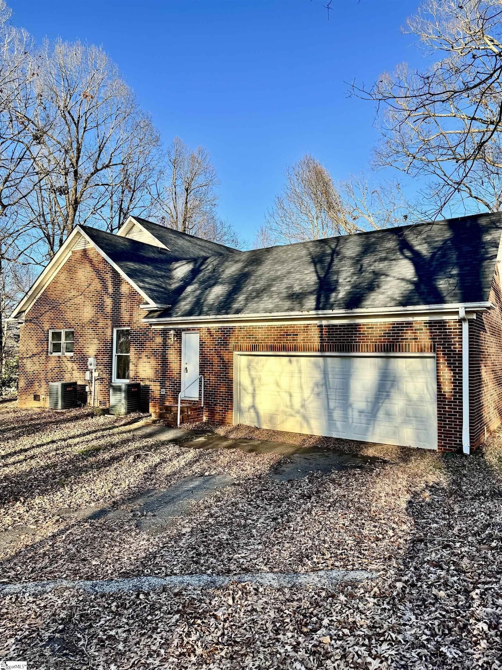 view of side of property featuring a garage, driveway, central AC, and brick siding