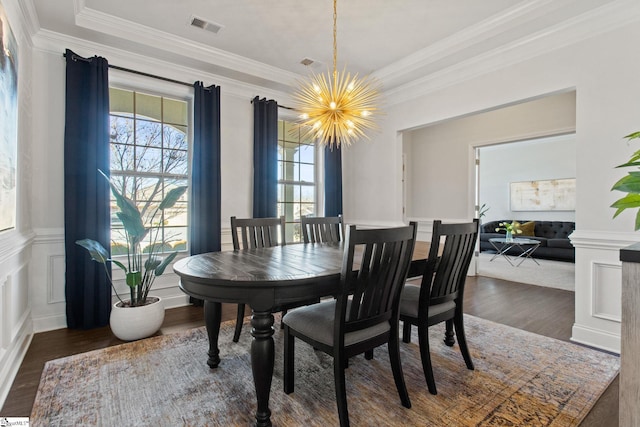 dining area with a chandelier, a decorative wall, wood finished floors, visible vents, and crown molding