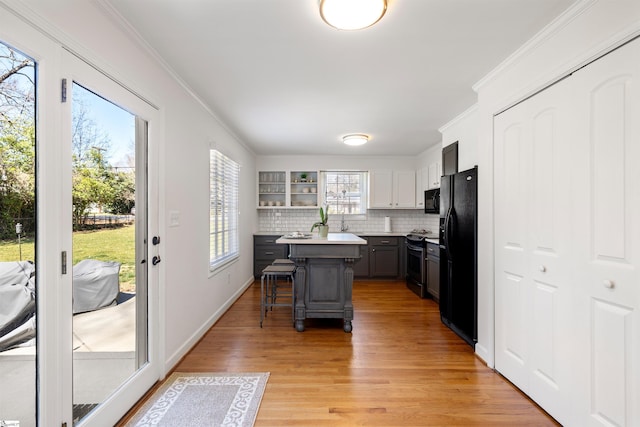 kitchen with black appliances, ornamental molding, light countertops, and a kitchen breakfast bar