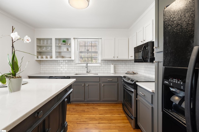 kitchen with gray cabinetry, a sink, light wood-style floors, light countertops, and black appliances