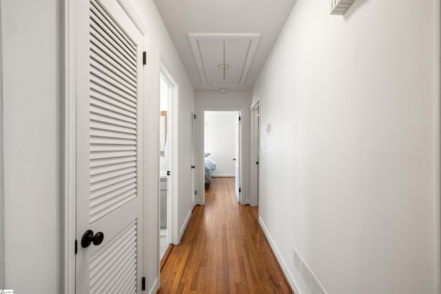 hall featuring attic access, baseboards, and wood finished floors