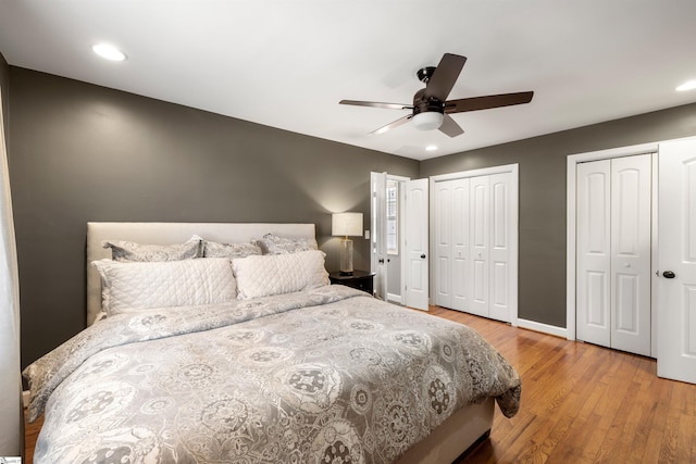 bedroom with recessed lighting, wood finished floors, a ceiling fan, baseboards, and multiple closets
