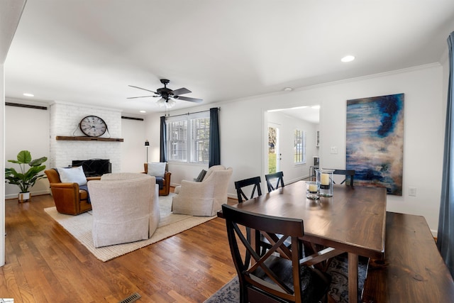 dining space featuring ornamental molding, a brick fireplace, and wood finished floors